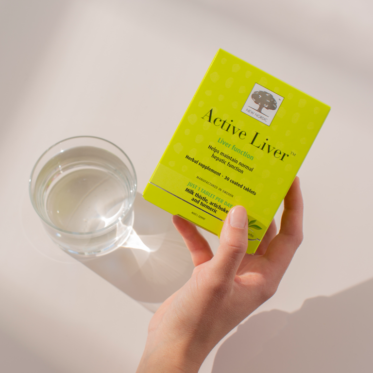 Hand holding the Active Liver™ package with a glass of water on the side.