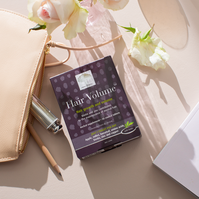 The Hair Volume™ package displayed with light pink roses and a bag.