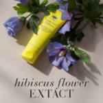The Gentle Face™ Exfoliator surrounded by purple hibiscus flowers with text hibiscus flower extract.