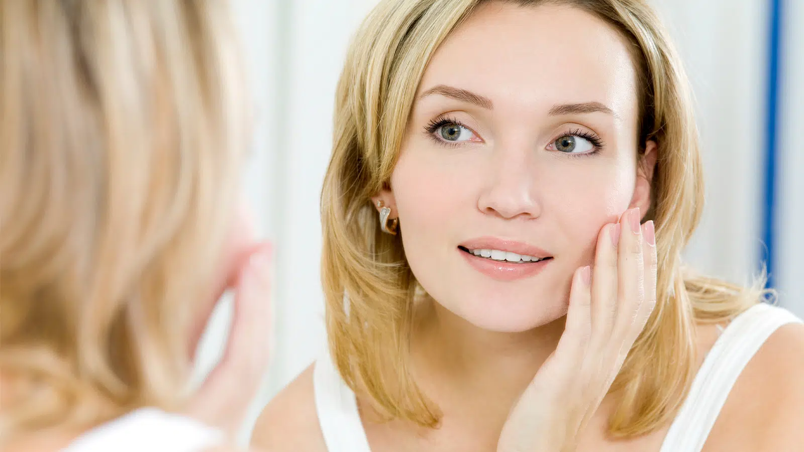 A woman examining her skin in the mirror.