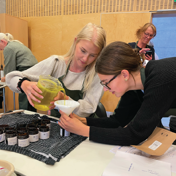 Two women experimenting with herbs at a herbal school event, learning about and engaging with plants.