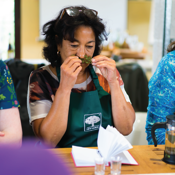 Woman smelling herbs at a herbal school event, engaging with plants and learning about their uses.